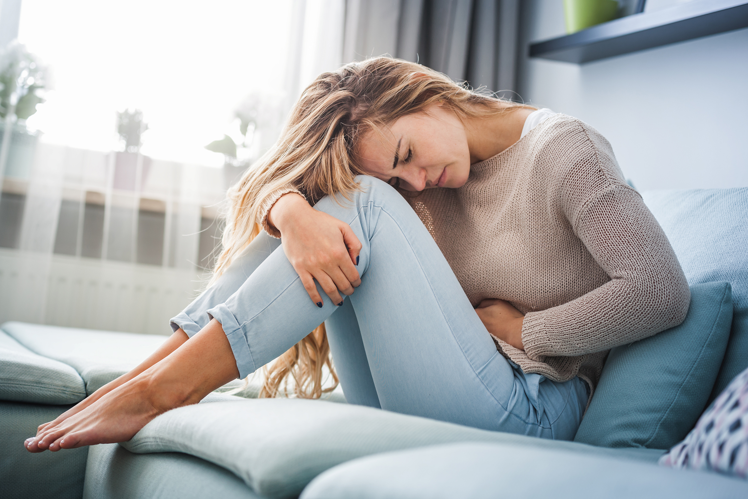 eine frau mit schmerzverzerrtem gesicht sitzt auf der couch und hält sich den bauch 